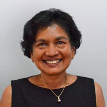 Sue is smiling at the camera; she has short black hair and is wearing a black top.
